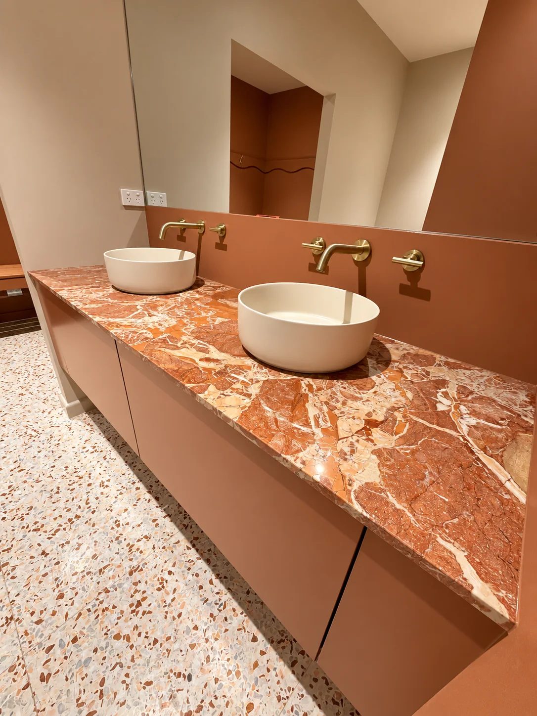 Twin above-counter basins on a stone benchtop with wall-mounted brass tapware