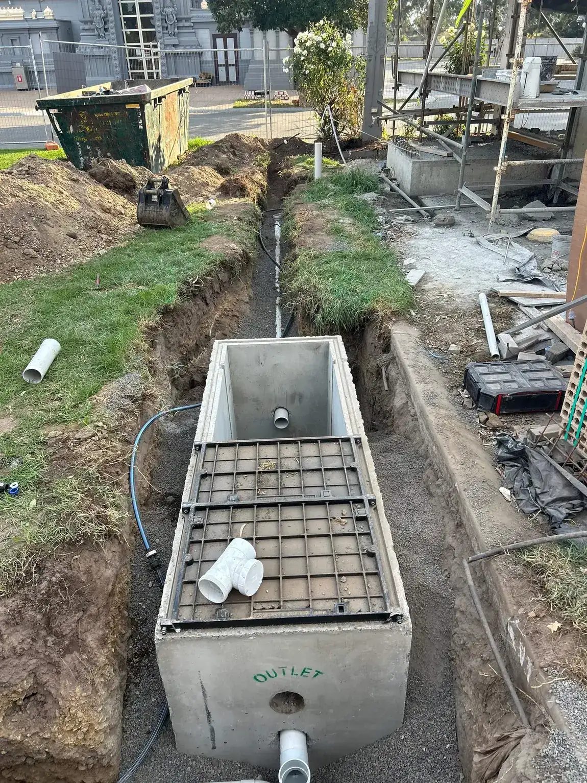 Trade waste tank set in excavation with outlet pipework connected and trench line running away